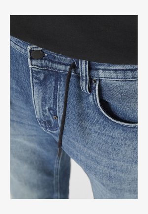 Blauwe denim jeans hebben een knoopsluiting, zwarte trekkoord en een voorzak, en tonen een vervaagde wassing en een zachte textuur.