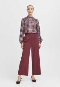 Cămașă cu mânecă lungă în carouri roșii și albe, cu front butonat, asortată cu pantaloni largi bordeaux. Botine cu accent de fundiță.