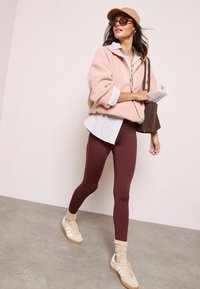 Roosa fliispullover, triibuline teksashirt, kurgiroheline retuus, kreemikad sokid ja heledad tennisetossud. Aksessuaaridena on beež müts ja prillid.