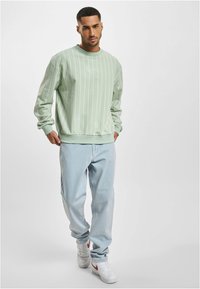 Light green sweatshirt with white vertical stripes, round neckline, and ribbed cuffs, paired with light blue jeans and white sneakers with red accents.
