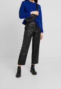 Niebieski sweter z dzianiny o teksturowanym wzorze, w połączeniu z błyszczącymi czarnymi skórzanymi spodniami prostymi oraz czarnymi botkami za kostkę.