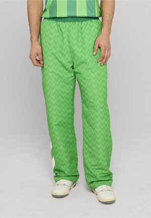 Zielone spodnie dresowe z wzorem w jodełkę, posiadające elastyczny pas i białe boczne paski. Noszone z białymi trampkami.
