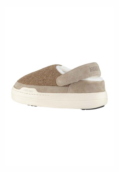 Bruin vilten en suede pantoffel met een ronde vorm, verstelbare band en witte fleece voering, geplaatst op een gestructureerde roomkleurige zool.