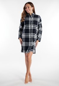 Vestido camisero de franela en un patrón de cuadros azul marino y blanco, con cuello tipo camisa, mangas largas, tapeta de botones y aberturas laterales.