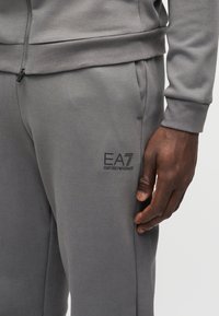 Γκρι φόρμα από απαλό ύφασμα, με κεντημένο λογότυπο EA7 σε μαύρο χρώμα. Σχεδιασμένη με τσέπες και ελαστικές μανσέτες για άνεση.