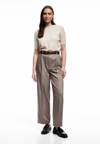 Creme gebreide trui met korte mouwen, geplooide lichtbruine broeken met een bruine riem met een gouden gesp, en zwarte loafers.