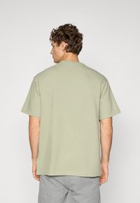 Korte mouwen, ronde hals t-shirt van lichtgroene textuurstof, met een ontspannen pasvorm en zijnaad. Draagt met grijze trainingsbroek.