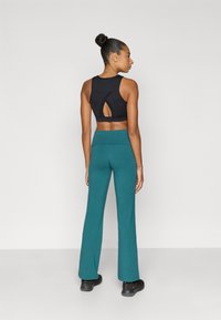 Μαύρο αθλητικό σουτιέν με λεπτομέρεια ανοίγματος στην πλάτη, συνδυασμένο με πετρόλ φαρδύ παντελόνι και μαύρα αθλητικά παπούτσια. Μεταξένιο ύφασμα και άνετη εφαρμογή.