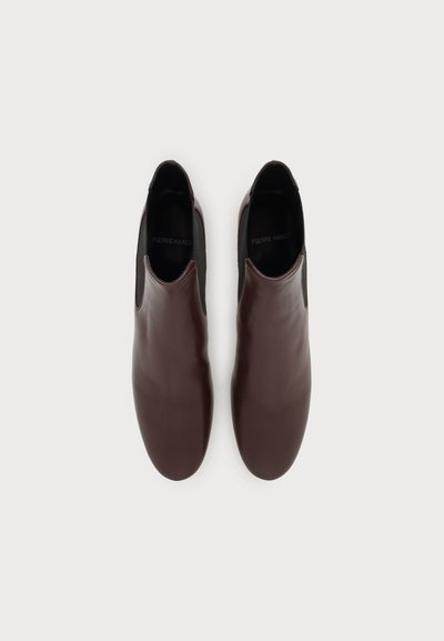 Paire de chaussures en cuir marron foncé à enfiler avec des panneaux latéraux élastiques noirs, vues de dessus sur un fond clair uni.
