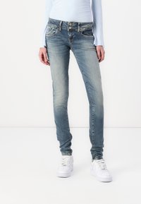 Skinny jeans made of faded blue denim, featuring a two-button fly, front pockets, and subtle whiskering, paired with white sneakers.