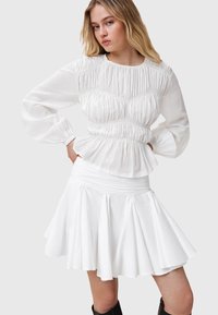 Witte katoenen blouse met geplooide details en lange mouwen, gecombineerd met een bijpassende flairrok met een geplooide tailleband en plooien.