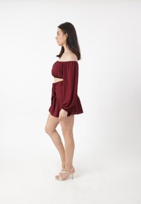 Bordeaux to-delt outfit bestående af en off-the-shoulder bluse og en nederdel med en bånddetalje, parret med strappy højhælede sandaler.