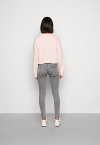 Felpa cropped rosa, jeans skinny grigi a fantasia e sneakers bianchi, vista da dietro, su uno sfondo grigio chiaro.