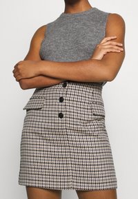 Szary bezrękawnik z dzianiny zestawiony z mini spódnicą w wzór houndstooth, ozdobioną czarnymi guzikami i bocznymi kieszeniami.