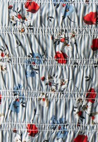 Tessuto a fantasia floreale con fiori rossi e blu su uno sfondo a strisce blu chiaro; presenta una texture arricciata con cuciture orizzontali.