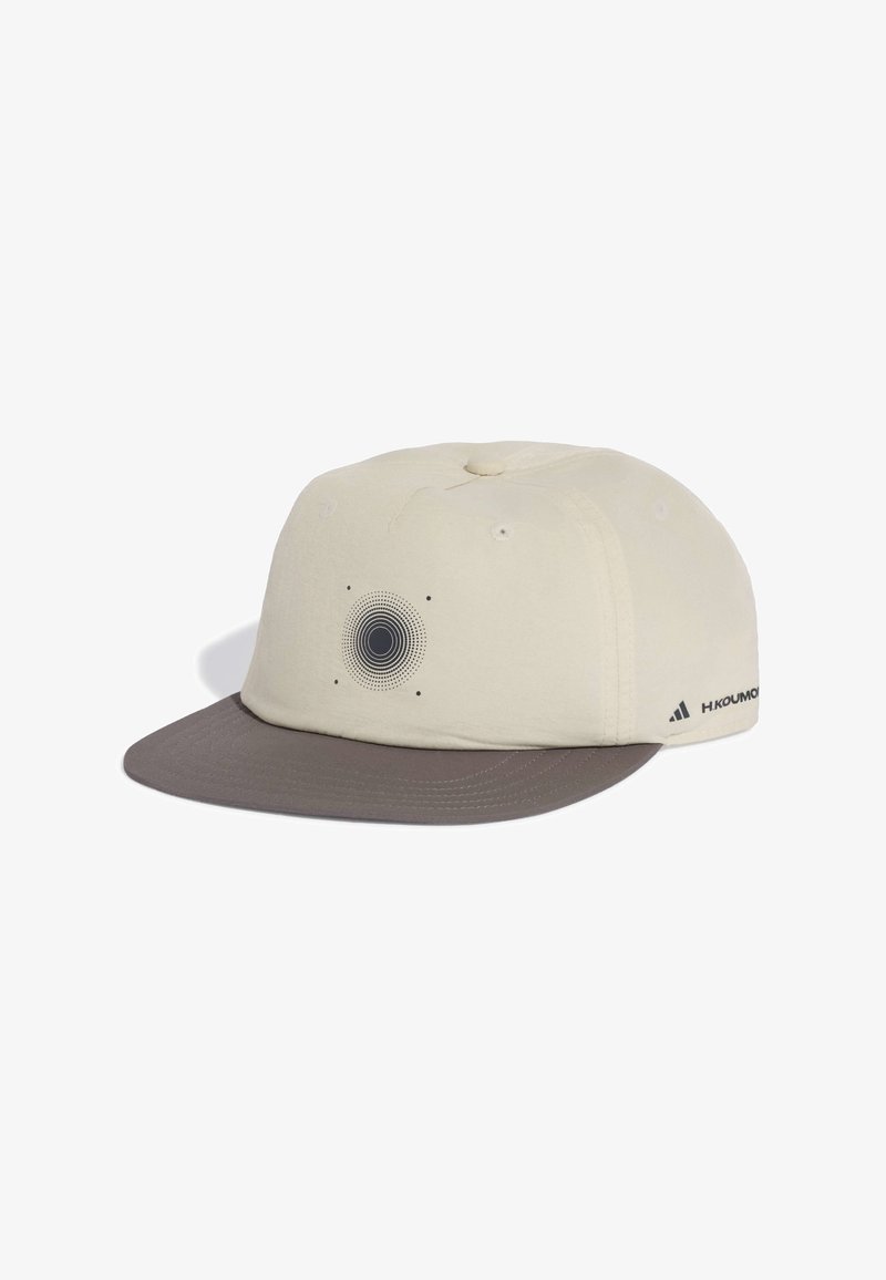 Casquette de baseball couleur crème avec une visière gris foncé, présentant un motif circulaire de points à l'avant et un petit logo sur le côté.