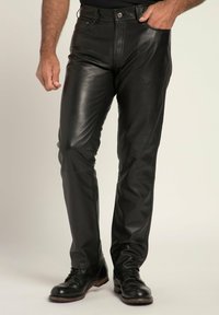 Schwarze Lederhosen mit einer figurbetonten Passform und leichtem Glanz, Fronttaschen und einem klassischen Bund. Getragen mit schwarzen Schuhen.