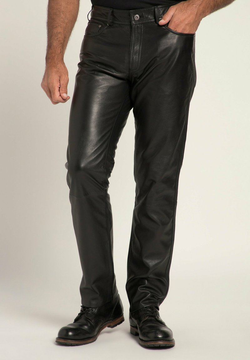 Schwarze Lederhosen mit einer figurbetonten Passform und leichtem Glanz, Fronttaschen und einem klassischen Bund. Getragen mit schwarzen Schuhen.