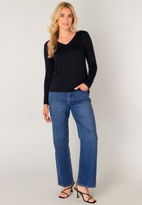 Marineblauw V-hals shirt met lange mouwen gecombineerd met hoog uitgesneden blauw rechte jeans en zwarte sandalen met bandjes, met een minimalistisch ontwerp en een gladde textuur.