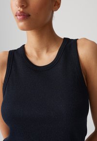 Top senza maniche a coste di colore blu navy con scollatura rotonda, che mette in mostra una superficie testurizzata e una silhouette aderente, evidenziando un tessuto morbido e elasticizzato.