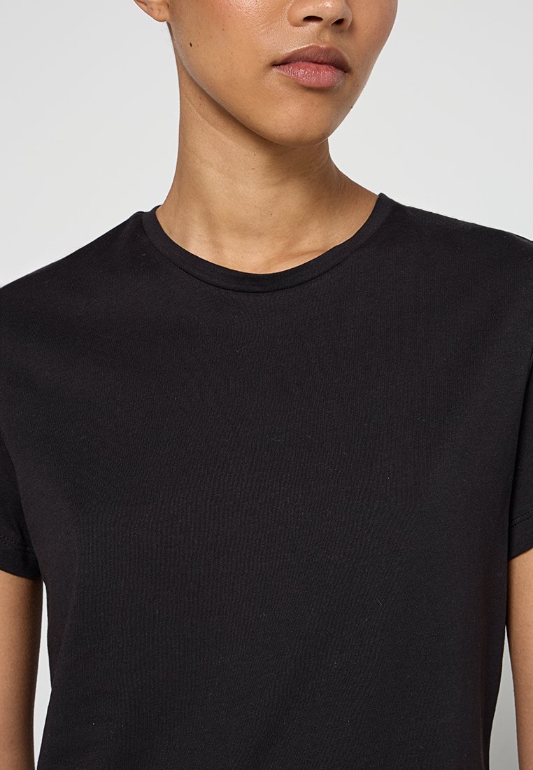 Camiseta de algodón negra con cuello redondo y mangas cortas, con una textura suave y detalles acanalados a lo largo del cuello.