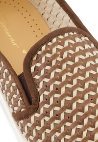 Brown woven slip-on shoe featuring a textured upper with geometric patterns, a brown trim, and a smooth inner lining.