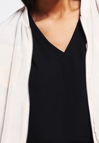 White zippered jacket over a black V-neck top. The jacket features a smooth texture, while the top has a matte finish.