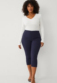 Top bianco a maniche lunghe con scollatura a V, abbinato a leggings capri blu navy. I leggings hanno una finitura liscia e un design a vita alta. Sandali neri con tacco.