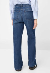 Donkerblauwe spijkerbroek met een rechte snit, voorzien van twee achterzakken en een taille op heuphoogte. De stof heeft een subtiele textuur.