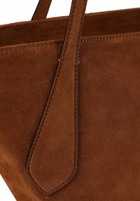 Braune Wildleder-Handtasche mit glatter Textur, einem zulaufenden Riemen und präzisen Nähten entlang der Kanten.