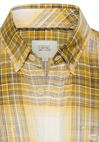 Duży kołnierz koszuli w żółto-brązową kratę zapinanej na guziki, z widoczną metką "Camel Active" od wewnątrz.