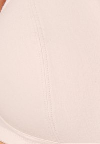 Reggiseno imbottito beige con texture di stoffa liscia, caratterizzato da un design senza cuciture e dettagli di cucitura sottili. Forma curvata per un supporto ottimale.