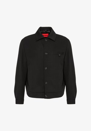 Black button-up jacket with collar, long sleeves, and a small buttoned pocket on the left chest. Red "HUGO" tag inside collar.