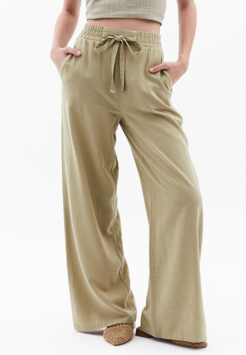 Licht olijfgroene wijde broek gemaakt van een zachte, gestructureerde stof. Heeft een elastische tailleband met een trekkoord en zijzakken.