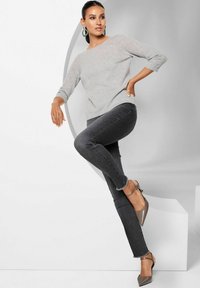 Hellgrauer, langärmeliger Pullover kombiniert mit dunkelgrauen Jeans mit ausgefransten Säumen. Das Model trägt braune, spitze Absatzschuhe mit Knöchelriemen.