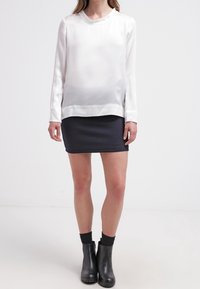 Vit satin långärmad topp med rundad halsringning, i kombination med en mörk texturerad minikjol och svarta ankelboots.