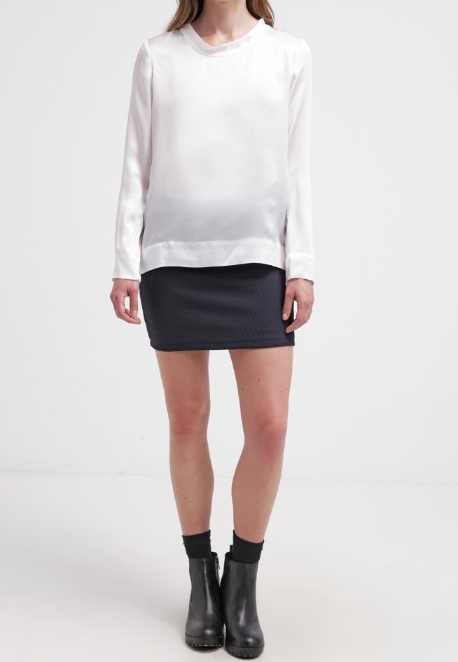 Vit satin långärmad topp med rundad halsringning, i kombination med en mörk texturerad minikjol och svarta ankelboots.