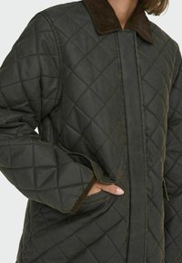 Giacca trapuntata verde scuro con colletto in corduroy marrone, caratterizzata da cuciture diagonali, tasche laterali e chiusura frontale con zip.