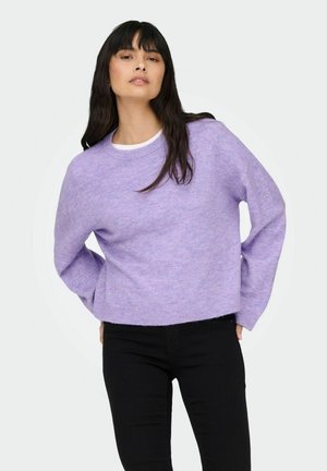 Pull lilas texturé avec un col rond et des épaules tombantes. Comprend des manches longues et une coupe décontractée, porté avec un pantalon noir.