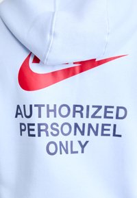 Világoskék kapucnis pulóver, nagy piros Nike logóval és fekete felirattal, amely így szól: "CSAK ENGEDÉLYEZETT SZEMÉLYEKNEK". Puha anyag, texturált felülettel.