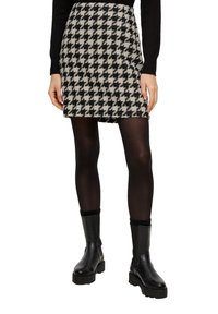 Mini-rok met houndstoothpatroon in zwart en crème, gemaakt van textuurstof, gecombineerd met zwarte panty’s en chunky enkelboots.