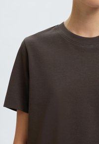T-shirt di cotone marrone scuro con colletto girocollo classico, maniche corte e una consistenza liscia e uniforme. Design minimalista, senza motivi o dettagli visibili.