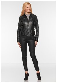 Schwarze Lederjacke mit tailliertem Design, Reißverschluss und vier Fronttaschen. Kombiniert mit schwarzen Skinny-Hosen und Stiefeletten.