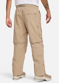 Beiga cargobyxor med avslappnad passform, elastisk midja, flera sidofickor och sömnadsdetaljer. Bärs med beiga sneakers.