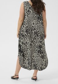 Femme portant une robe midi sans manches à imprimé léopard, associée à des escarpins à talons kitten noirs, se tenant de dos face à l'appareil.