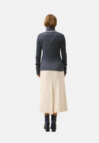 Marineblauer, gerippter Rollkragenpullover mit enger Silhouette, kombiniert mit einem cremefarbenen Midikleid mit einem Schlitz hinten. Getragen mit schwarzen, hohen Stiefeletten.