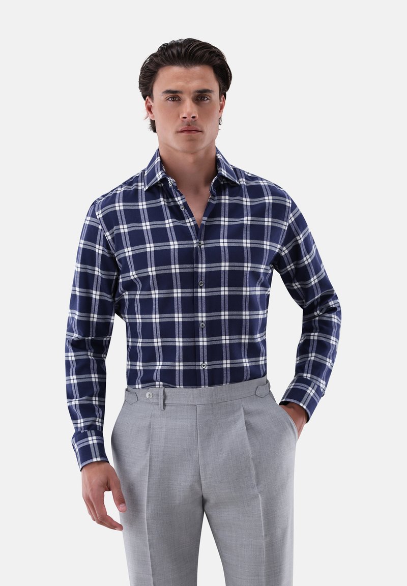 Camicia a scacchi blu e bianca con maniche lunghe e colletto abbottonato, abbinata a pantaloni grigi chiari con frontale piatto e tasche laterali.
