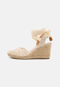 Sandale espadrille à talon compensé beige avec un dessus en crochet, une sangle autour de la cheville et une semelle en jute tissée au fini texturé.