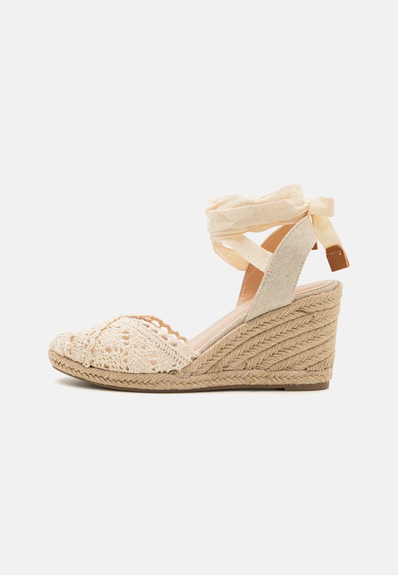 Sandale espadrille à talon compensé beige avec un dessus en crochet, une sangle autour de la cheville et une semelle en jute tissée au fini texturé.