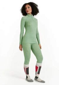 Maglia termica verde chiaro a maniche lunghe con zip a metà e leggings abbinati. Presenta motivi testurizzati. Calzini grigi e rossi con accenti distintivi.